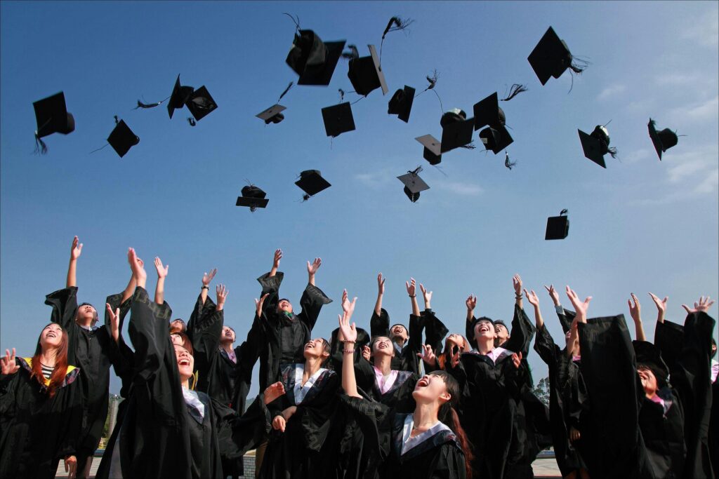 Group of graduates celebrating by throwing caps in the air during a sunny day.